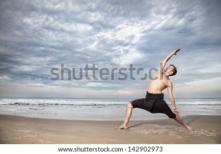 Yoga warrior pose by man in black trousers on the beach near the ocean in India