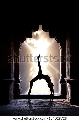 Man silhouette doing yoga in old temple at sunset sky