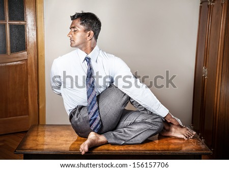 Indian businessman doing yoga on the table in the office