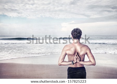 Man doing Namaste behind his back and looking to the ocean