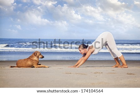 Woman in white costume doing Yoga and looking at the dog on the beach near the ocean in India