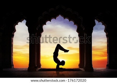 Man silhouette doing yoga advance scorpion pose in old temple at orange sunset sky background