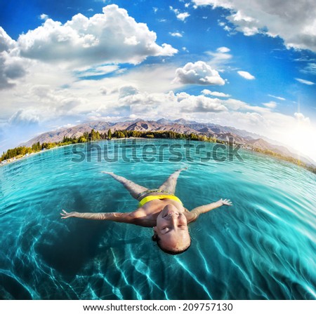 Woman laying like a star in Issyk Kul lake at mountains background in Kyrgyzstan, central Asia