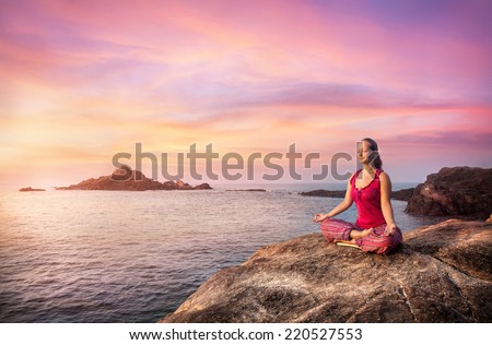 Woman doing meditation in red costume on the stone near the ocean in Gokarna, Karnataka, India