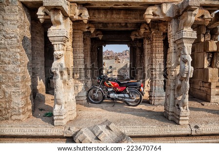 HAMPI, KARNATAKA, INDIA - MARCH 12, 2013: Red motorbike parked in ancient temple with columns in Hampi kingdom complex