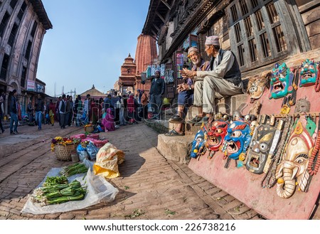 BHAKTAPUR, KATHMANDU VALLEY, NEPAL - APRIL 9, 2014: Two old men sitting on the stairs near mythological wooden masks at the street market