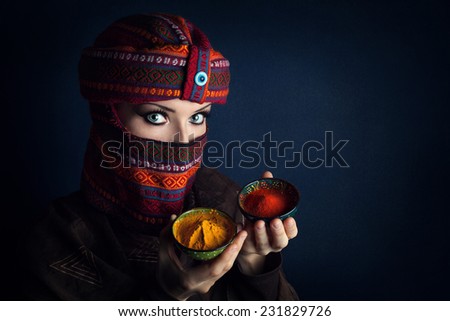 Oriental woman in turban offering red chili and yellow turmeric powders at bazar