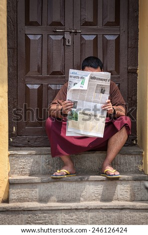 SWAYAMBHUNATH, KATHMANDU, NEPAL - APRIL 5, 2014: Buddhist monk sitting on the steps and reading the local newspaper on Nepali language