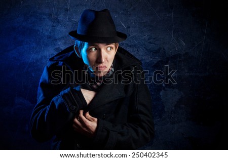 Man in black hat put out something from his coat at dark background