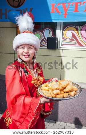 ALMATY, KAZAKHSTAN - MARCH 22, 2015: Woman in red national Kazakh costume holding baursak national food at Nauryz celebration