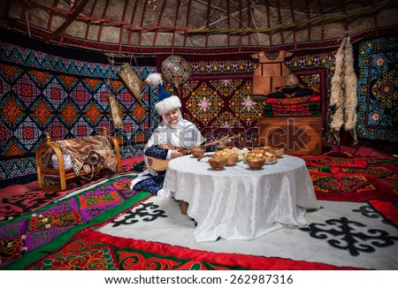 ALMATY, KAZAKHSTAN - MARCH 22, 2015: Woman in national Kazakh costume with dombra music instrument near the table with national food in Yurt nomadic house at Nauryz celebration