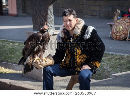 ALMATY, KAZAKHSTAN - MARCH 22, 2015: Man in national Kazakh costume holding falcon big bird with eyes closed by hat at Nauryz celebration