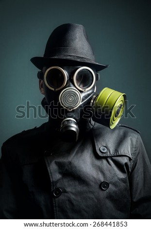 Man in gas mask, raincoat and black hat at dark background