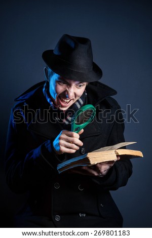 Emotional man in black hat with magnifier glass reading the old book at dark background