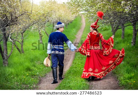 Couple in Kazakh costume walking around Spring Blooming apple garden of Almaty, Kazakhstan, Central Asia