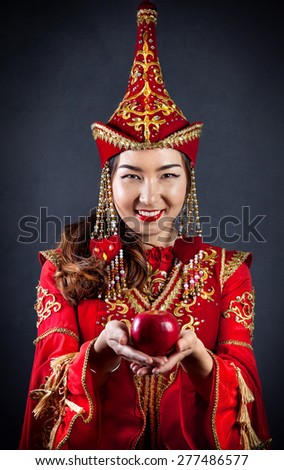 Woman in red national Kazakh costume holding red apple at grey background