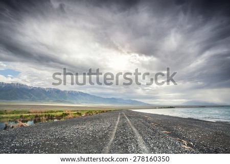 Road near Alakol Lake and mountain scenery at dramatic overcast sky in Kazakhstan, central Asia