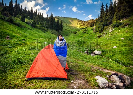 Tourist in sleeping bag near orange tent in the mountains in Kazakhstan, central Asia