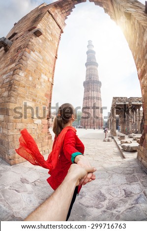 Woman in red costume leading man by hand to Qutub Minar tower in Delhi, India
