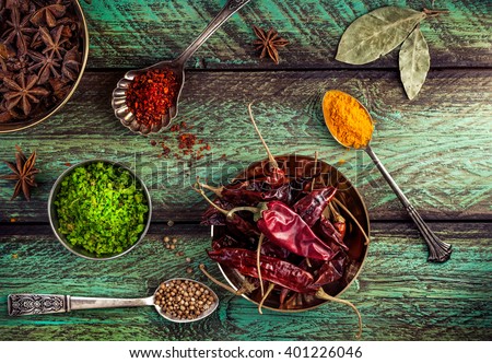 Spices, dry red chili peppers at wooden green background with spoons nearby