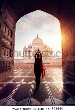 Woman doing yoga tadasana tree pose with flying red scarf in silhouette near Taj Mahal in Agra, Uttar Pradesh, India