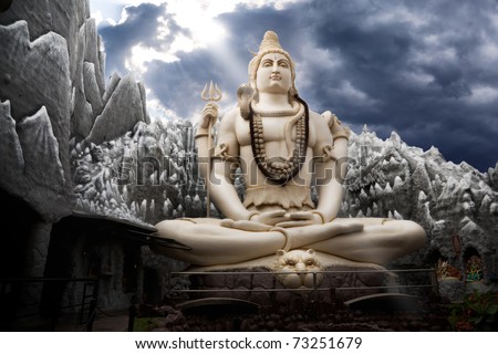 Big Lord Shiva statue sitting in lotus with trident in his hand and cobra near by. Dramatic sky at background with ray on Shiva. Bangalore, India