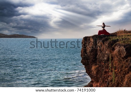 Beautiful woman doing virabhadrasana warrior yoga pose on the cliff near the ocean with dramatic sky at background in India