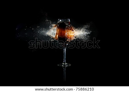 Glass with brown liquid exploded by bullet with many splashes around at the black background