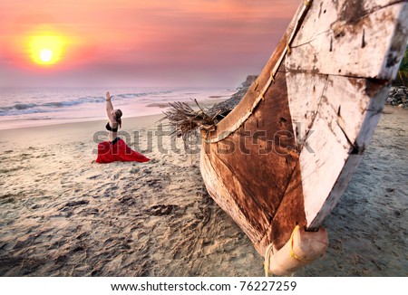 Beautiful woman doing virabhadrasana warrior yoga pose on the beach near the ocean on sunset in India