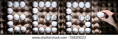 Word EGG from white eggs in the box and hand holding one egg