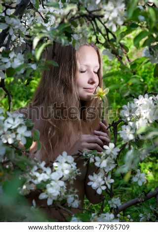 Young beautiful woman smelling yellow narcissus flower with eyes closed around white flowers