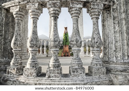 Yoga shirshasana, head stand pose is done by Indian man in green trousers between stone columns at mountain background