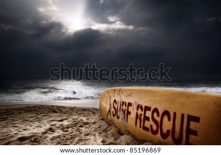 Surfboard with title surf rescue on the beach near the ocean at dramatic storm sky with dark clouds background
