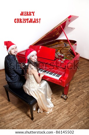 Christmas party with Man and woman in Christmas hats playing the piano and smiling with wine glasses and red rose on the red grand piano. Free space for text