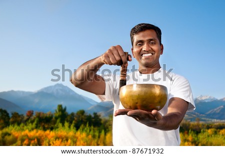 Yoga meditation practice with singing Tibetan bowl by happy Indian Man in white cloth in the morning at mountain background
