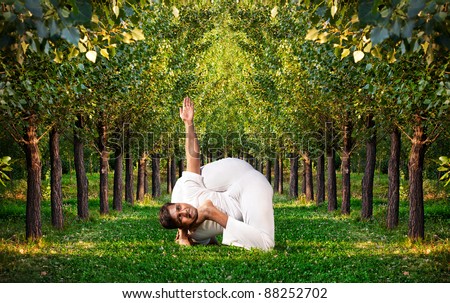 Yoga bal krishnasana difficult pose by Indian man in white cloth. Green trees around him