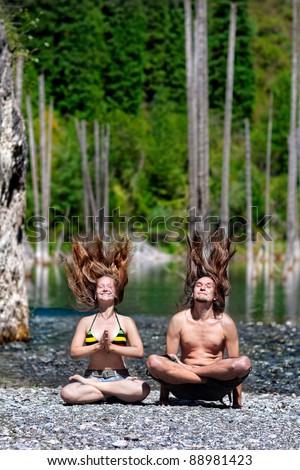 Yoga couple meditation in padmasana pose by happy Man and woman with hair up on the stone beach at nature background