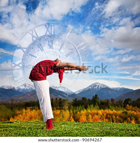 Christmas yoga Hasta Uttanasana backward bending pose by Indian man in white trousers, red socks and Christmas hat at clock and nature background