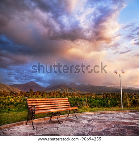 Lonely bench in the park with lamppost nearby at mountain and sunset dramatic sky background. Presidents park in Almaty, Kazakhstan