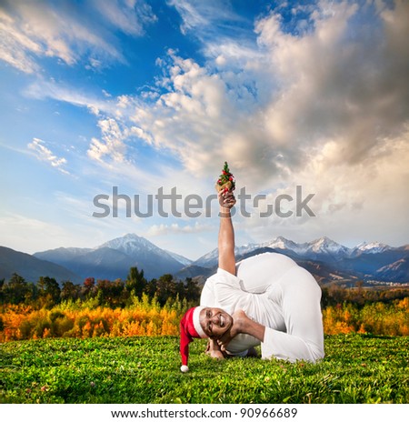 Yoga bal krishnasana pose by Indian man with Christmas tree in white cloth and Christmas hat at mountain background