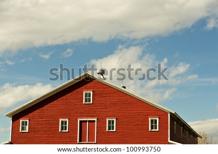 Top of a red barn with white trim and weather vanes on a beautiful spring day