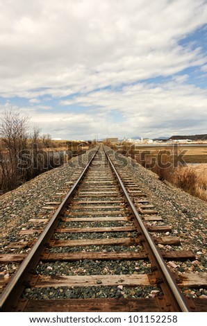 Railroad tracks running straight past an industrial area and then disappearing in the distance where blue mountains can be seen