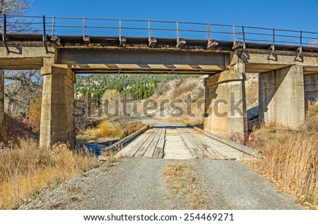 Railroad bridge over a gravel road and a wooden bridge that spans a creek