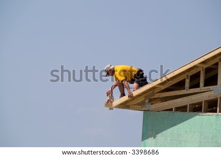 Construction worker using circular saw on roof of new home to trim excess from edge of roof