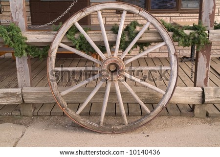 Wagon wheel leaning against a fence with a touch of green looks appealing, feels inviting