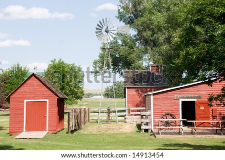 Aeromotor windmill used to pump well water stands between red farm buildings