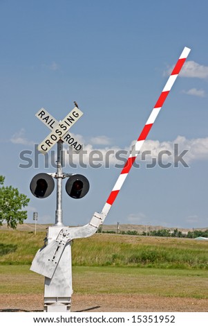 Railroad crossing signal with lights, barrier, and a bird on the sign at a museum