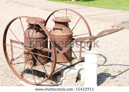 Rusty antique metal milk cans on a wooden cart with rusty metal wheels