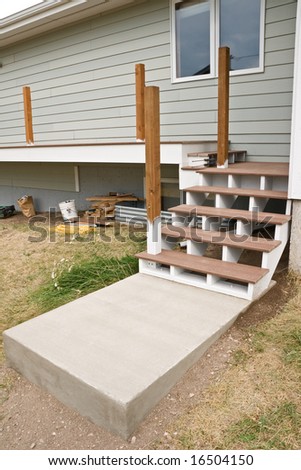 New composite steps on wood base with new concrete slab and new composite deck with treated wood posts before railing