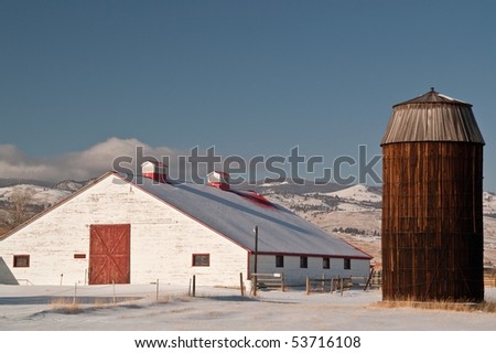 Vintage wooden silo and horse barn with peeling paint and red metal roof covered with snow - focus on silo